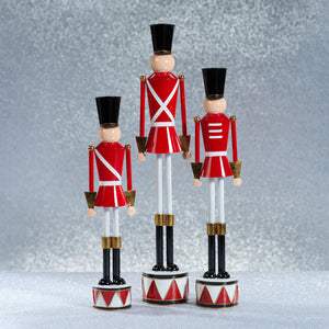 The ZODAX ALLOY FESTIVE DECORATIVE SOLDIER - TALL features a classic nutcracker style with alloy accents, a red coat, white straps, gold details, and stands upright on a small drum base for a modern festive touch.