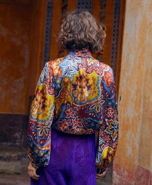 The MOMONI - THIERRY BLOUSE IN PRINTED STRETCH SATIN is a long-sleeved, oversize silk blouse with a multicolored paisley and floral print, high pleated collar, and buttoned cuffs, shown on a plain white background.