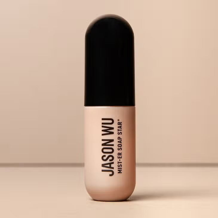 A beige and black cylindrical bottle of JASON WU BEAUTY&#39;s &quot;MIST-ER SOAP STAR BROW SOAP&quot; is centered against a neutral background. The minimalistic design features black text on the front, enhancing its sleek aesthetic.