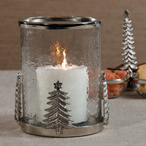 A ZODAX GLASS & ALLOY HURRICANE 8″ featuring a metallic base and silver Christmas tree accents, containing a lit white pillar candle.