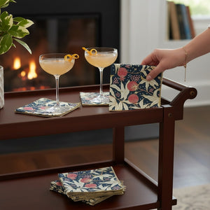 The DOT AND ARMY Gooseberry Cocktail Napkin features a red, cream, and dark green floral and pomegranate print with yellow-stitched edges—sustainable napkins ideal for any gathering.