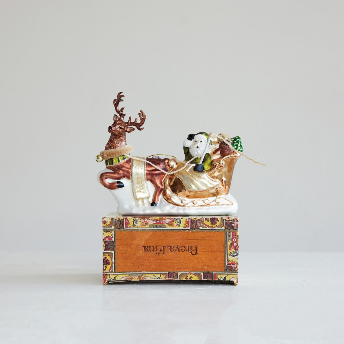 Creative Co-op Hand-Painted Glass Santa’s Sleigh and Reindeer Ornament with glitter, showing Santa in a sleigh being pulled by a reindeer.