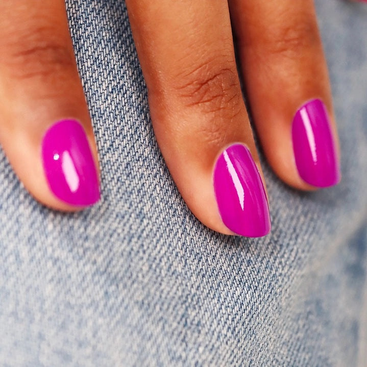 A close-up of MANUCURIST - GREEN™ NAIL POLISH IN ARMERIA by MANUCURIST INC being spread with a brush on a smooth surface, showcasing its vibrant pinky mauve shade, glossy texture, and distinctive curved brushstroke.