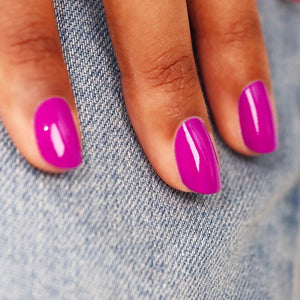 A close-up of MANUCURIST - GREEN™ NAIL POLISH IN ARMERIA by MANUCURIST INC being spread with a brush on a smooth surface, showcasing its vibrant pinky mauve shade, glossy texture, and distinctive curved brushstroke.