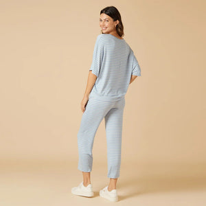 A woman wears the SOFTIES Dream Relaxed V-Neck with Capri Lounge Set in Sky Blue Stripe, featuring soft jersey fabric, short sleeves, matching drawstring capri pants, and white sneakers for a relaxed, all-day comfortable look.