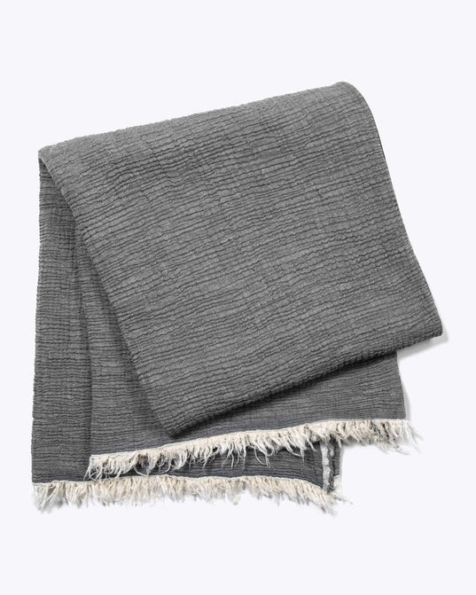 The MERSEA CLOUD GAUZE BLANKET is a folded, textured gray cotton throw with a ribbed pattern and off-white fringe along the edges, shown against a plain light background.