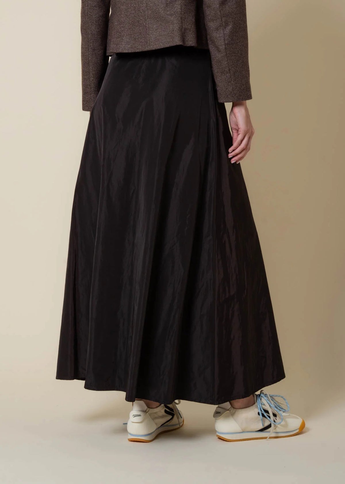 A person wearing a white sweater has their hand in the pocket of the VICARIO CINQUE GRANADA Taffeta Skirt in Marron Brown, a high-waisted skirt crafted from memory taffeta with a subtle sheen.