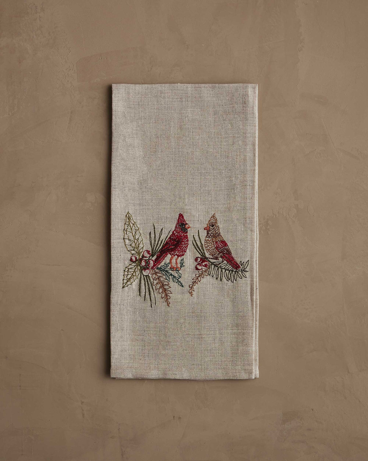 A CORAL & TUSK CHRISTMAS CARDINALS LINEN TEA TOWEL made of embroidered natural flax fiber featuring two cardinals perched on pine branches with berries.