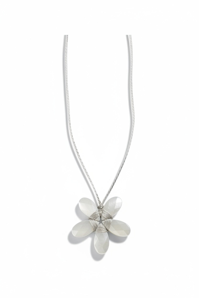 A white mannequin is dressed in a curly beige faux fur coat and adorned with the ANN LIGHTFOOT - SMALL MOTHER OF PEARL FACETED FLOWER NECKLACE by ANN LIGHTFOOT. The softly blurred background features light-colored walls and window blinds.