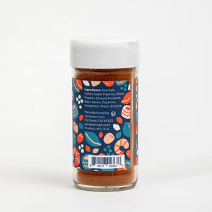 A 2.6 oz jar of JACOBSEN SALT CO. Seafood Seasoning, featuring a blue label adorned with vibrant seafood illustrations, white text, and a white lid. This seasoning is crafted with premium sea salt and an expertly balanced blend of herbs and spices—the label describes it as “An aromatic and savory everyday blend.”.