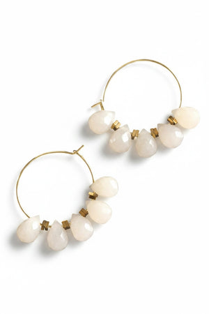 The DAVID AUBREY - DYED JADE MINI HOOP EARRINGS feature gold-plated hoops embellished with five teardrop-shaped, opaque white stones on each side, gracefully suspended from the hoops and displayed on a dark textured surface. Delicate gray jade beads from DAVID AUBREY accentuate the design, infusing these statement earrings with an elegant touch.