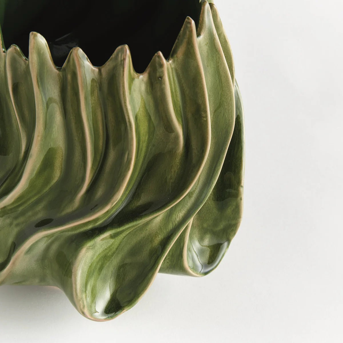 The NAPA HOME AND GARDEN - GREEN CALLISTA VASE, MEDIUM features a sculptural design with glossy green handcrafted ceramic, showcasing wavy, flame-like edges and ridges that evoke the look of abstract leaves or flames. A high-gloss reactive glaze accentuates its flowing, organic exterior shapes, while the interior is finished in a rich dark green.