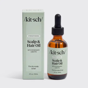 A person with long, brown, wet hair holds a dropper bottle labeled “KITSCH - Strengthening Hair & Scalp Oil” against their bare shoulder. The label highlights rosemary and is designed for dry scalp and hair, featuring ingredients like argan oil to support scalp health.