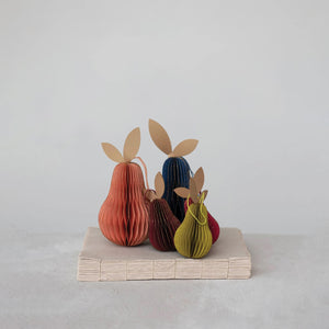 Five HANDMADE RECYCLED HONEYCOMB PAPER PEAR ORNAMENTS by CREATIVE COOP, featuring vibrant colors and textured paper leaves, are displayed atop beige books against a plain light gray background.