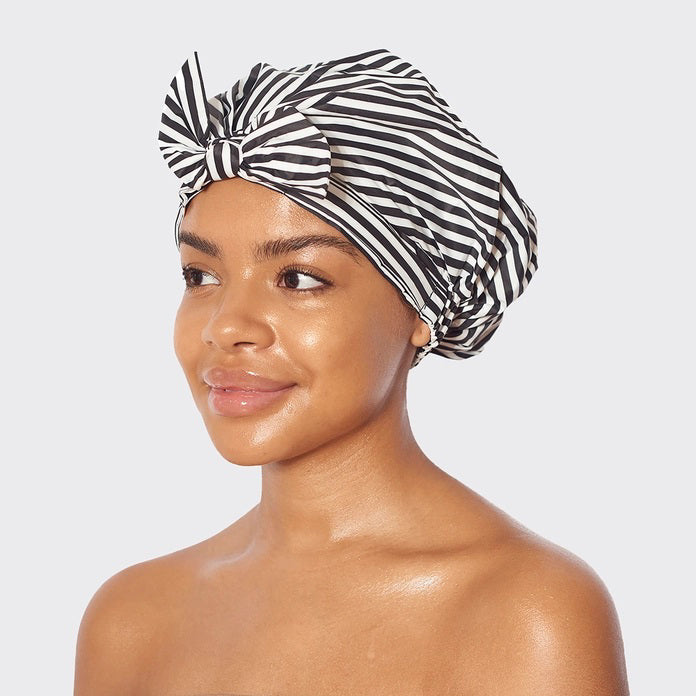 The KITSCH - LUXURY SHOWER CAP, with chic black and white stripes, is elegantly showcased in a pink box. The packaging highlights its waterproof, no-slip grip features and charming illustrations, complemented by a model's photo demonstrating its beauty.