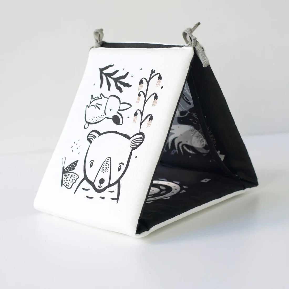 A TUMMY TIME GALLERY soft book from WEE GALLERY, featuring black and white fish and squid illustrations, is partially inserted in a clear front pocket. A brown tag attached by a string reads "tummy time gallery." This Montessori toy, ideal for sensory development, rests on a plain white surface.