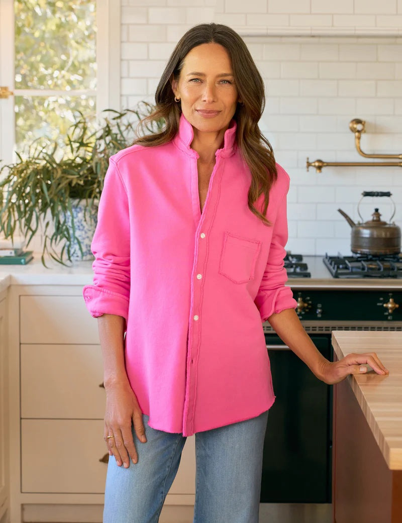 A woman with wavy brown hair wears the FRANK &amp; EILEEN EILEEN Relaxed Sweatshirt Button Up in Lotus, featuring white buttons and a chest pocket, standing indoors with part of her face visible.