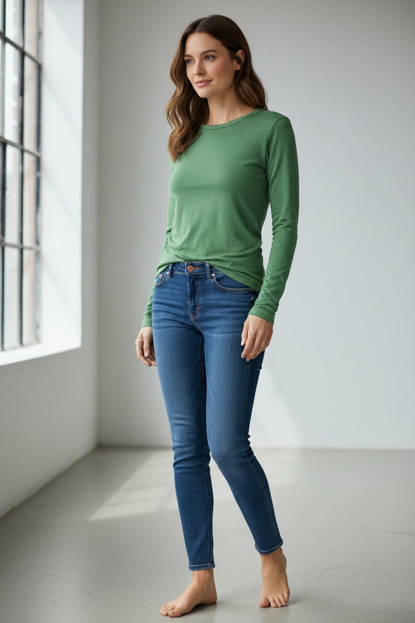 A woman with straight dark hair wears the KINROSS CASHMER Long Sleeve Crew Neck Silk Cashmere Sweater in light blue and white pants, standing against a plain light background with one hand in her pocket, looking at the camera.