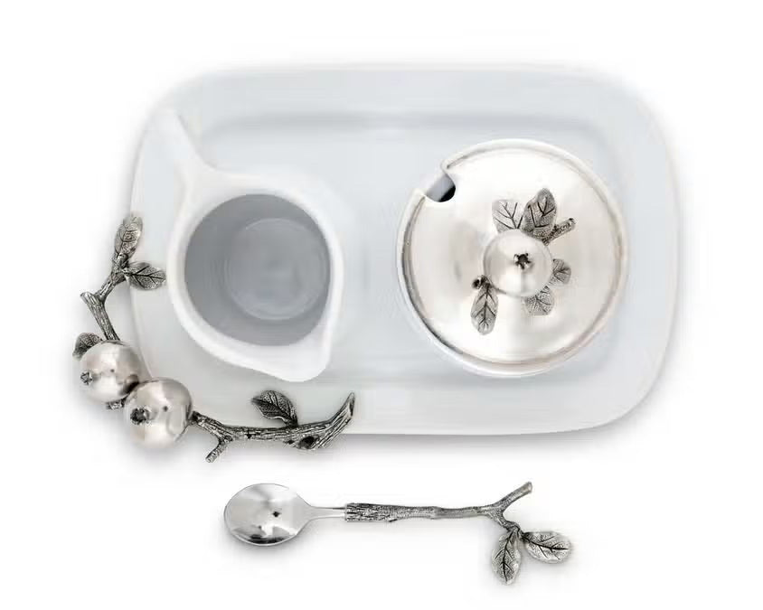 The VAGABOND HOUSE POMEGRANITE CREAMER SET includes a white ceramic sugar bowl with a metallic lid featuring pewter pomegranates, a matching cream pitcher, and a silver spoon with branch-like handle and pomegranate accents on a rectangular tray.