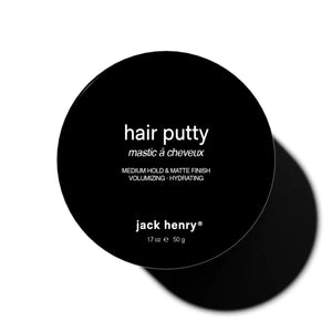 A round black container labeled "JACK HENRY - HAIR PUTTY" features white text promoting hydrating, volumizing benefits with medium hold and a matte finish. The Jack Henry container casts a shadow on a white background.