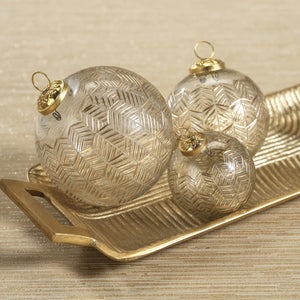 The ZODAX GOLDEN ECHOES ORNAMENT 4" is a clear glass Christmas ornament featuring a gold geometric leaf pattern, measuring 4 inches in diameter and hanging from a gold ribbon against a white background.