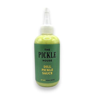 A plastic squeeze bottle featuring a green label with “THE PICKLE HOUSE - DILL PICKLE SAUCE” stands against a lightly textured backdrop—ideal as a tangy marinade or bold salad dressing from THE PICKLE HOUSE for your favorite recipes.