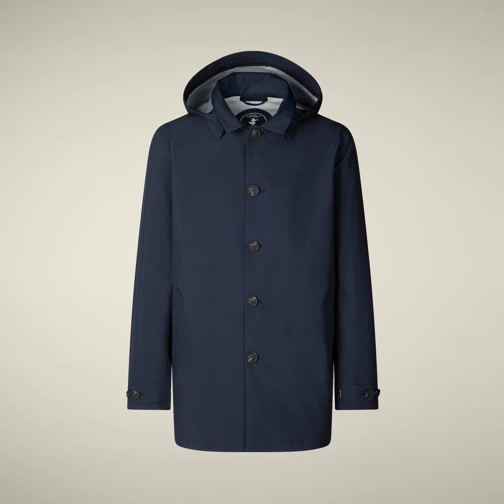 A person stands facing away, wearing the SAVE THE DUCK BENJAMIN Hooded Raincoat in Blue Black and loose tan corduroy pants against a plain light background.