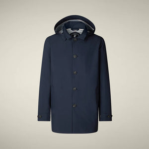 A person stands facing away, wearing the SAVE THE DUCK BENJAMIN Hooded Raincoat in Blue Black and loose tan corduroy pants against a plain light background.