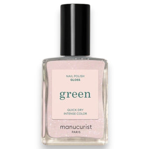 A bottle of MANUCURIST INC GREEN™ Nail Polish in Gloss, featuring a vegan, cruelty-free formula in a pale pink shade with a black cap. The label reads “green, quick dry intense color, nail polish gloss.”.