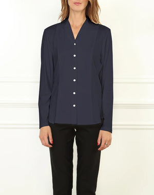A woman stands against a white wall, wearing the HINSON WU - DONNA Long Sleeve Wing Collar “T” Shirt in navy and black pants. Her hands are relaxed at her sides, and her face is partially out of frame.