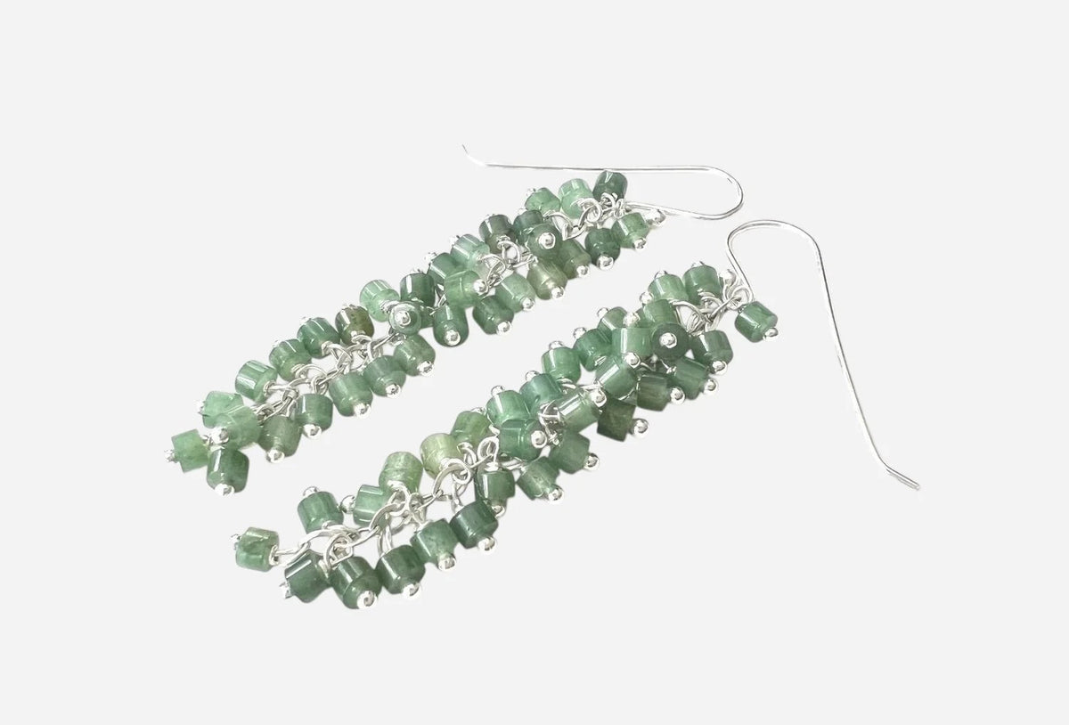 ANN LIGHTFOOT&#39;s Heishi Cut Green Aventurine Long Charm Earrings feature clusters of small green beads on sterling silver hooks, elegantly displayed on a dark rod.