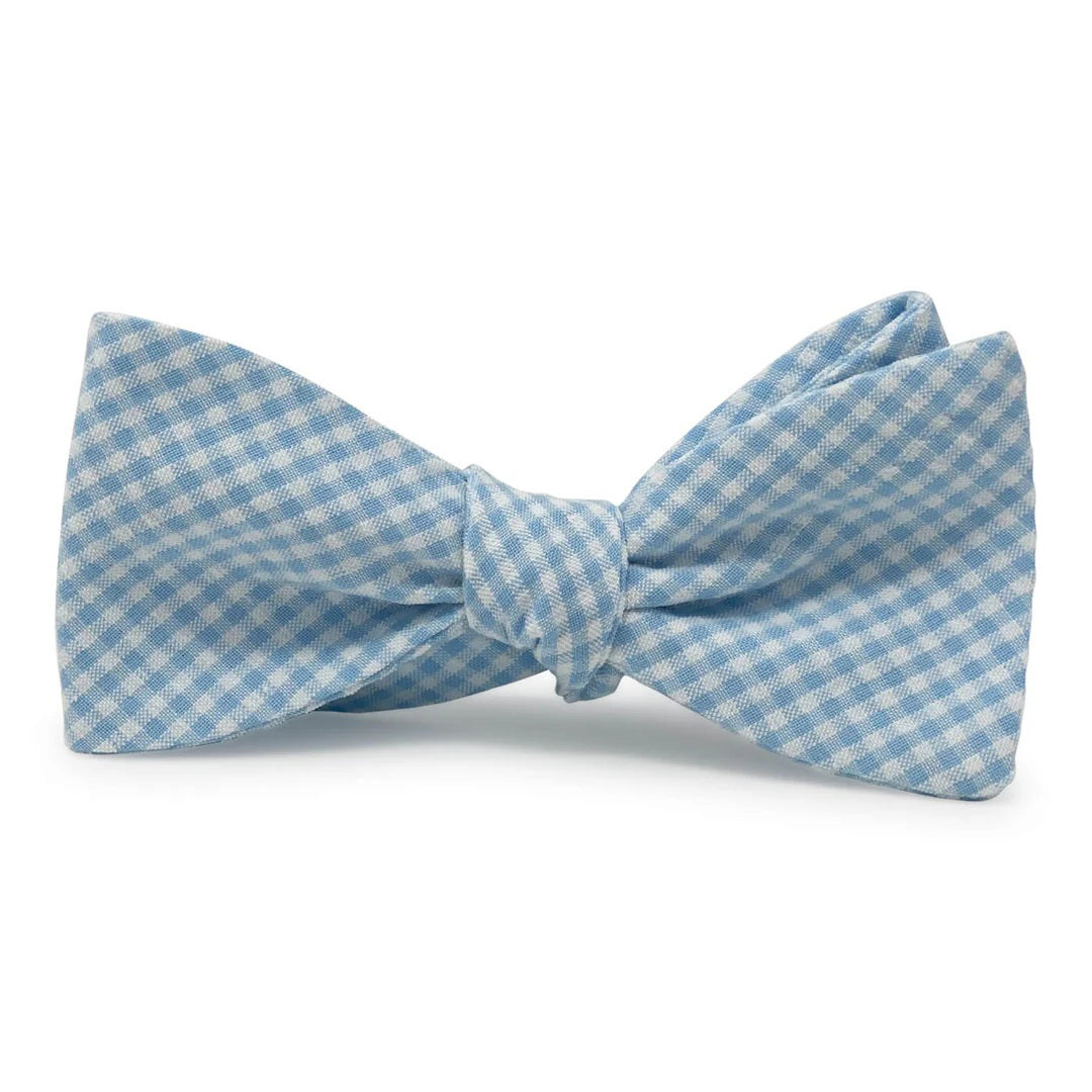 The COLLARED GREENS - FENWICK CAROLINA COTTON BOW TIE by BIRD DOG BAY features a neatly tied light blue and white gingham pattern, displayed on a plain white background.