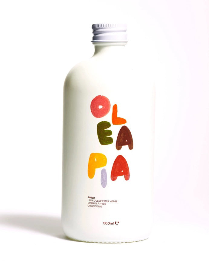 A 500-milliliter bottle labeled "OLEA PIA - BIMBO LIGURIAN OLIVE OIL" in colorful, playful letters is shown against a white background. This bottle contains organic extra virgin Ligurian olive oil made from Taggiasche olives, known for its sweet and fruity flavor.