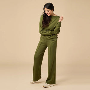 A woman wears a SOFTIES - DREAMTECH BOAT NECK WITH PINTUCK PANT SET in olive green, featuring a long-sleeve boat neck top and matching wide-leg pintuck pants.