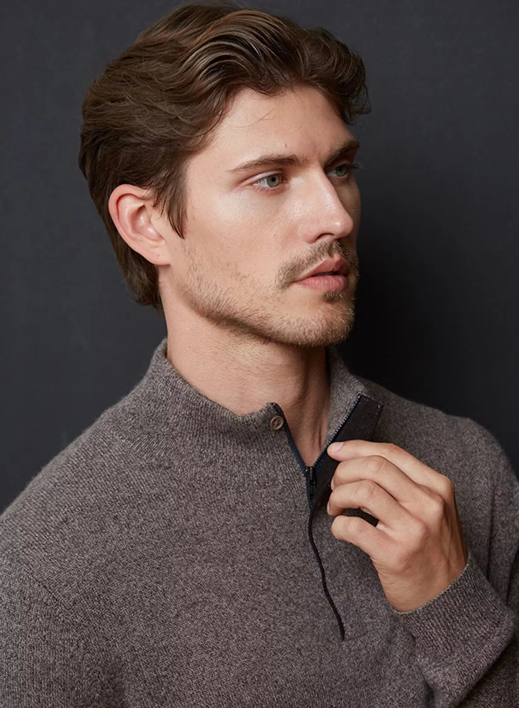 A man wearing a grey quarter-zip sweater, pulling the zipper.