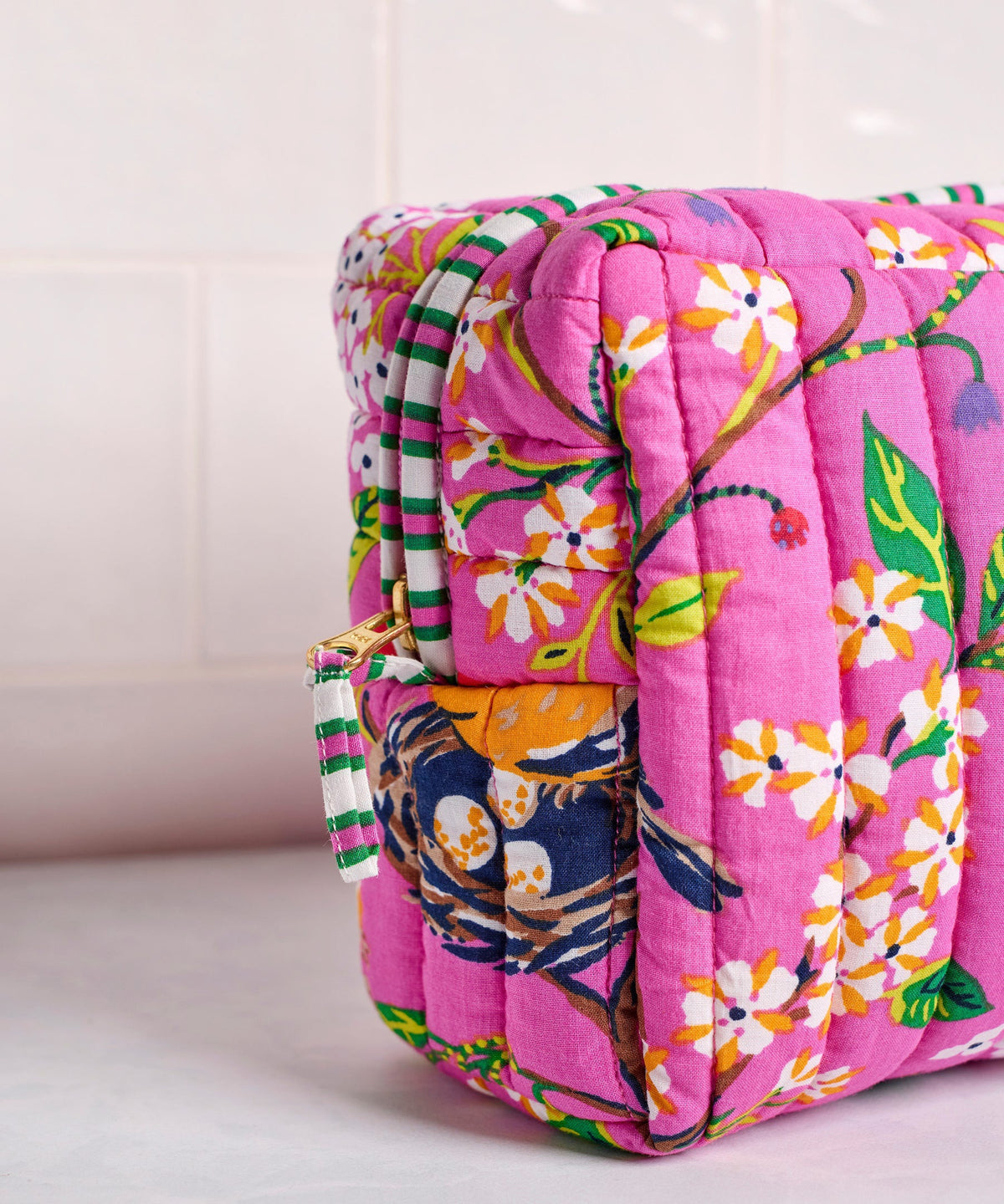 A person in a white shirt holds the PRINTFRESH - BIRD &amp; BLOSSOM THREE POUCH SET by PRINTFRESH, featuring three quilted makeup pouches with colorful floral and striped patterns, nested from smallest to largest.