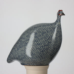 The LES CERAMIQUES DE LUSSAN - MEDIUM FRENCH GUINEA IN BLUE SPOTTED COBALT is a handmade ceramic sculpture featuring an intricate speckled pattern and distinctive red head detail. The predominantly white rounded body, adorned with black circular designs, echoes the appearance of guinea hens. Its plain white background highlights the artisanal charm of LES CERAMIQUES DE LUSSAN's craftsmanship.