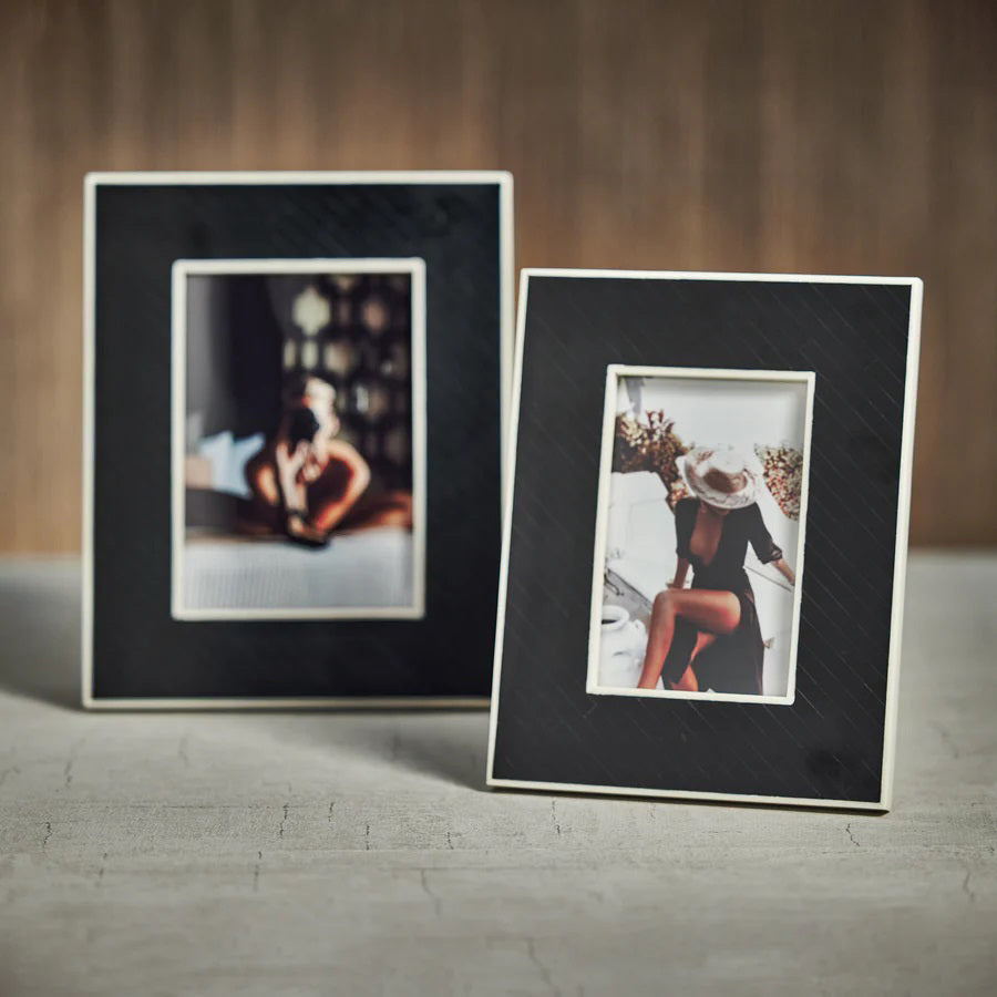 The ZODAX BLACK BONE INLAY WITH WHITE INNER BORDER is a black, rectangular 5x7 picture frame featuring a white inner border, shown upright against a white background displaying a photo of a person sitting on a bed.