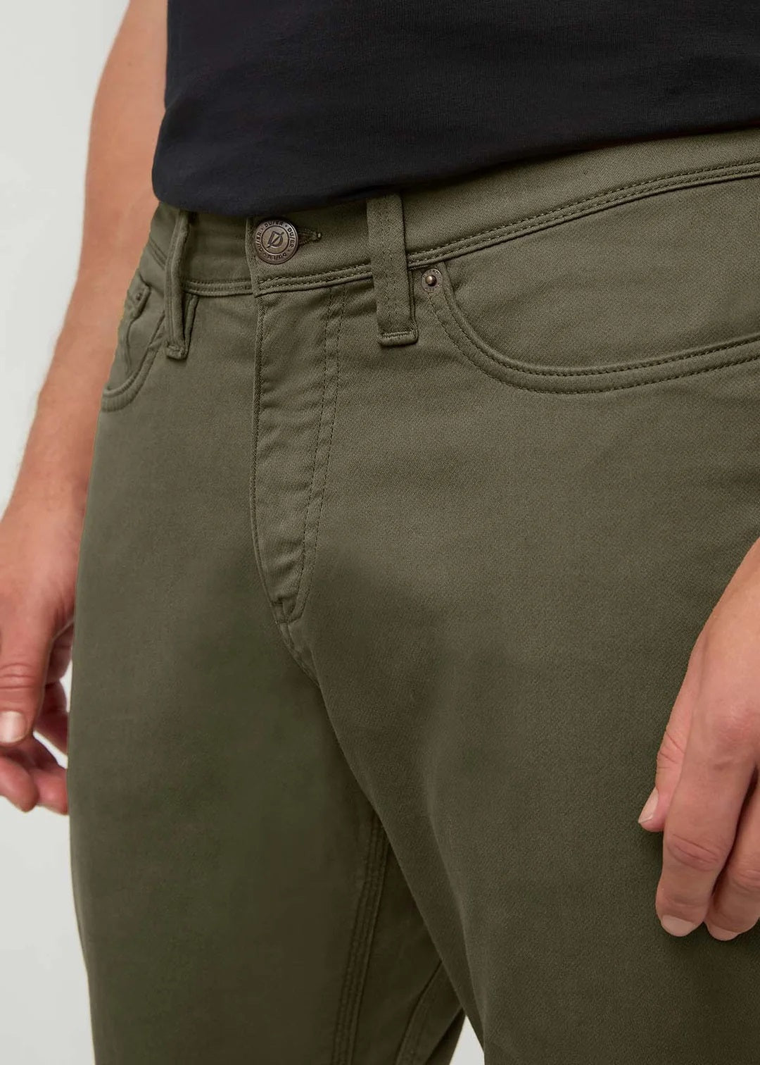 A person stands facing away from the camera against a plain background, wearing DUER - NO SWEAT ATHLETIC TAPER PANTS IN KELP paired with brown shoes.
