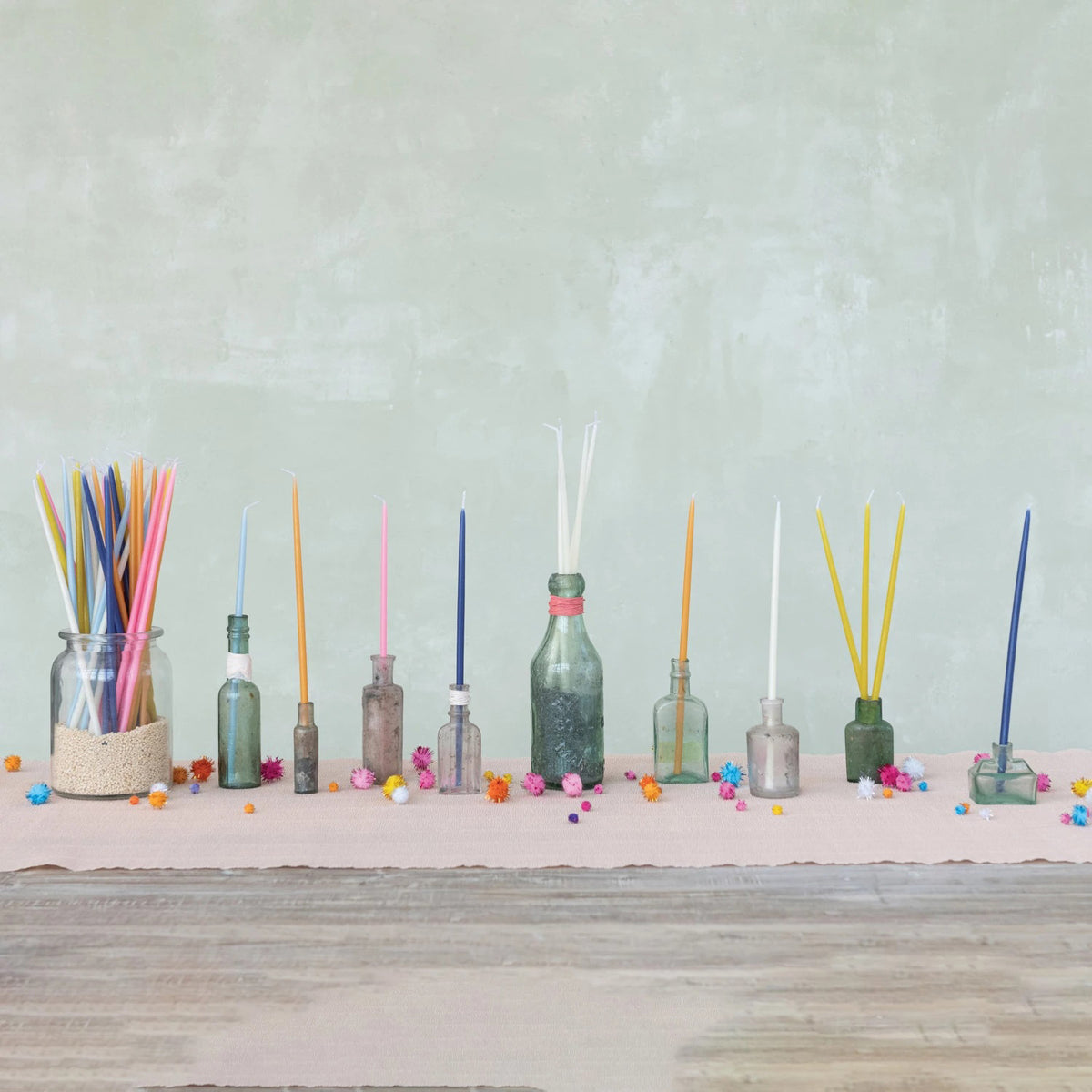 A set of CREATIVE COOP UNSCENTED THIN TAPER CANDLES in light blue, featuring white wicks, are shown arranged in a box and scattered outside it against a white background.