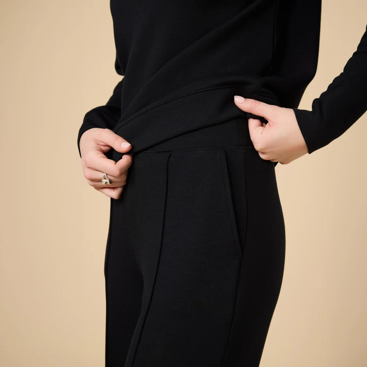 A woman wears a SOFTIES - DREAMTECH BOAT NECK WITH PINTUCK PANT SET in olive green, featuring a long-sleeve boat neck top and matching wide-leg pintuck pants.