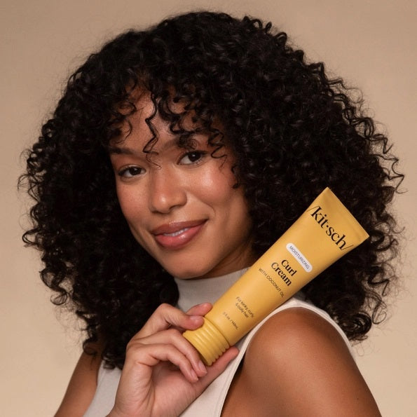 A yellow tube of KITSCH - MOISTURIZING CURL CREAM, formulated with coconut oil and designed for kinky, curly, and coily hair. This KITSCH brand curl cream is labeled as moisturizing and ideal for frizz control, with a smear of the product shown behind the tube.