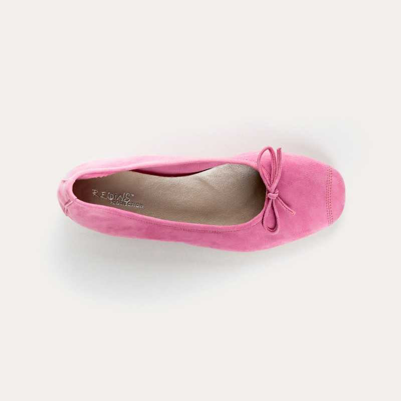 A close-up of the REQINS - HARMONY SUEDE BALLERINA FLATS IN PINK, featuring a bow detail on the front, photographed on a light surface—an elegant update to this classic women’s shoe by REQINS.
