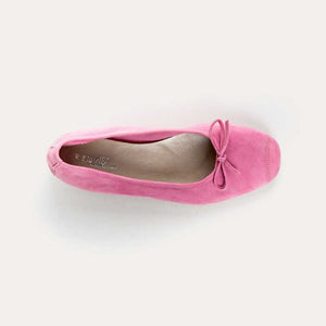 A close-up of the REQINS - HARMONY SUEDE BALLERINA FLATS IN PINK, featuring a bow detail on the front, photographed on a light surface—an elegant update to this classic women’s shoe by REQINS.