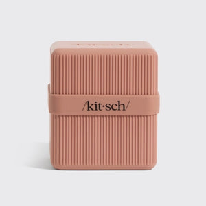 A terracotta, ribbed rectangular container with a matching lid slightly open and leaning against it. The lid features the word “kitsch” in black text. This TSA-approved KITSCH Two Compartment Travel Case is perfect for keeping your beauty essentials organized on the go.