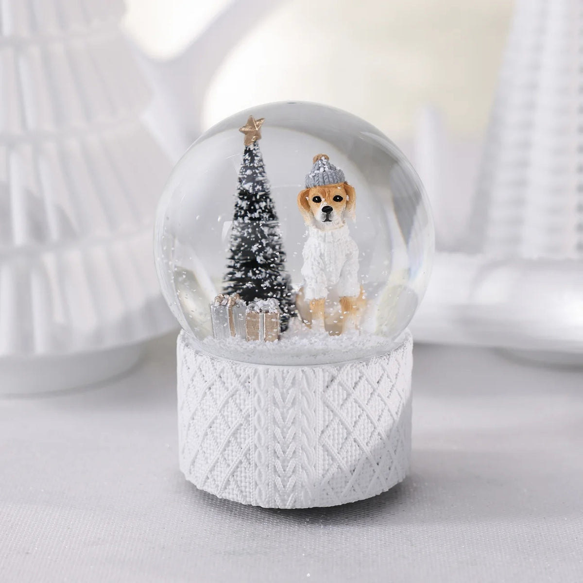 A ZODAX MOUNTAIN DOG WITH SWEATER SNOW GLOBE featuring a dog in a hat and sweater, a small Christmas tree, and gifts inside a resin glass ornament resting on a textured white base.