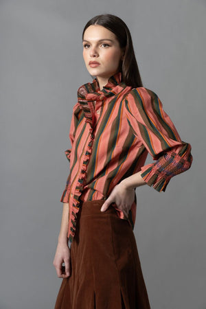 A woman models the HOPE FOR FLOWERS - FRILLED BUTTON DOWN SHIRT by HOPE FOR FLOWERS, made from GOTS certified organic cotton, with a high collar and wide sleeves, paired with flared blue jeans featuring fringe along the side seams.
