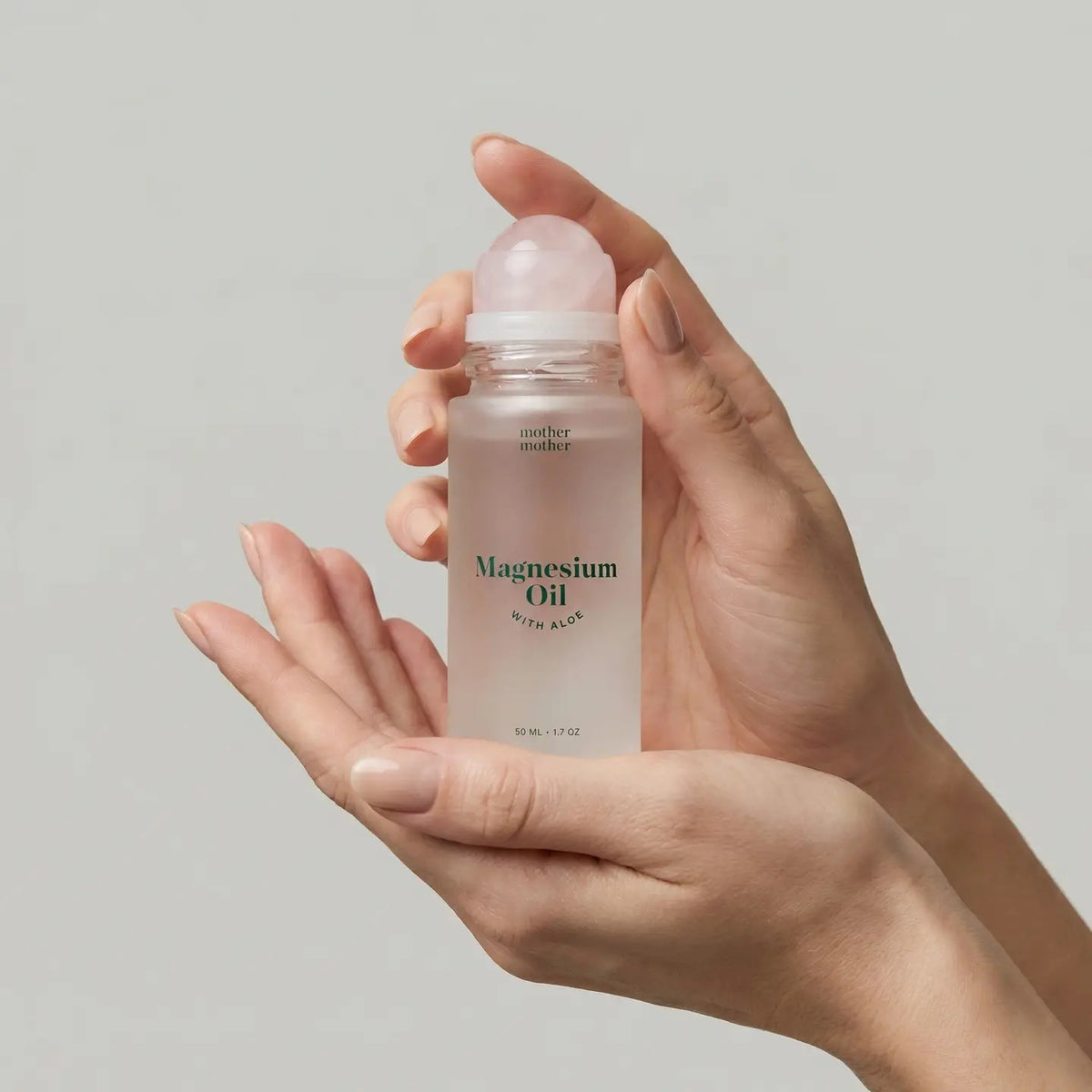 A green box and a frosted roll-on bottle of MOTHER MOTHER - MAGNESIUM OIL & ALOE ROLLER are displayed side by side. Designed for sensitive skin, the bottle from MOTHER MOTHER has its white cap removed and set to the right on a white surface.