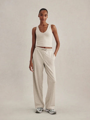 A woman wearing a light gray Varley Motion Easy Jogger 30 in Pebble Marl tank top and matching wide-leg joggers with athletic shoes.