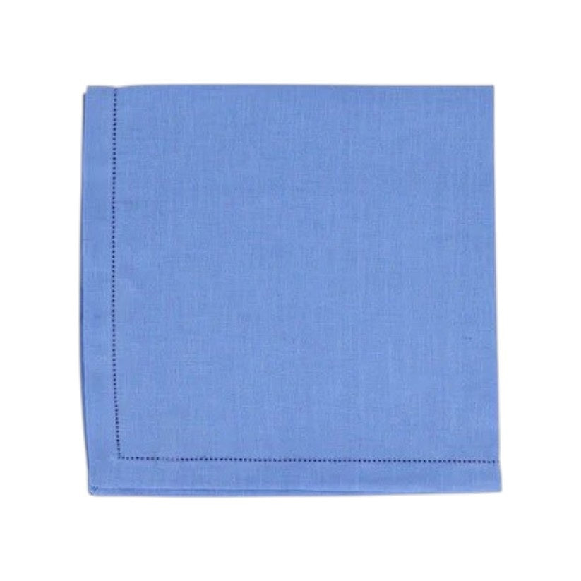 The VIETRI Tessuti Dinner Napkin in Cornflower Blue rests on a vibrant tablecloth with red, beige, and green geometric patterns outlined in white, bringing elegance to your VIETRI table linen collection.